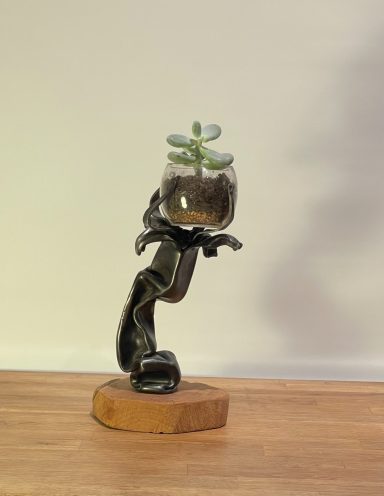 Sculpture en métal avec un pot de plante succulente sur un socle en bois.